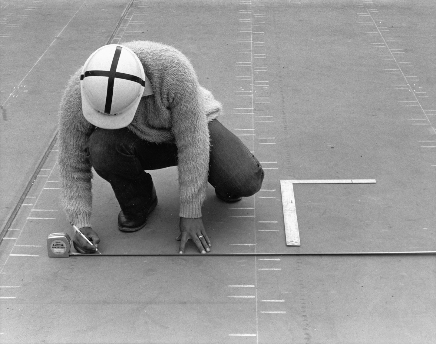Carpenter carefully marking lines on a large surface with tools.