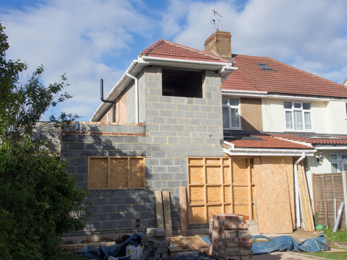 House extension under construction with concrete block walls and plywood windows.