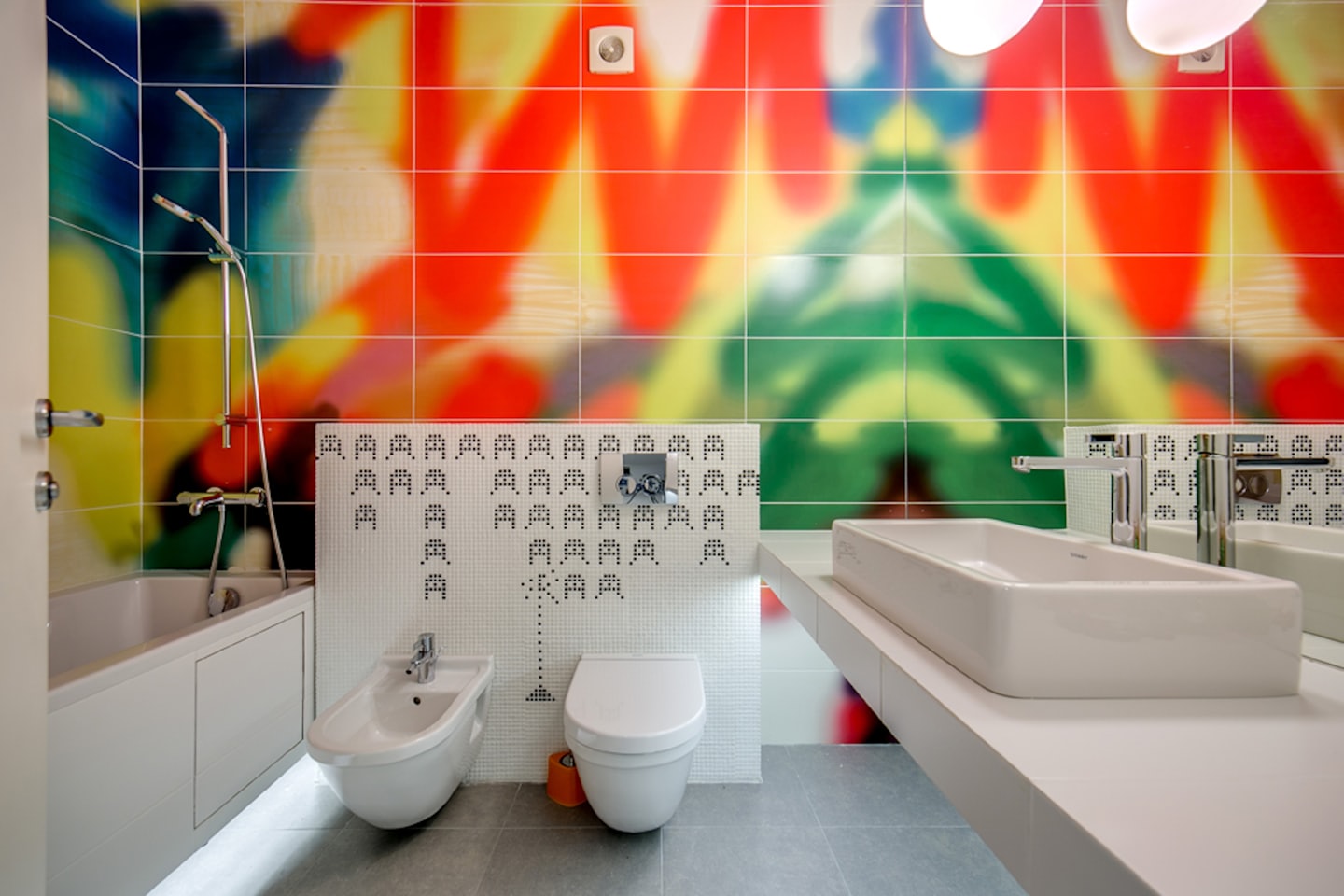 Modern bathroom with white fixtures and colorful patterned wall tiles.