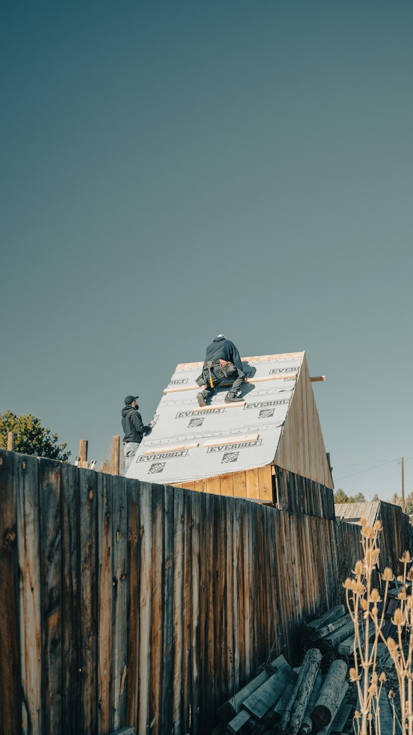 Construction workers building a wooden roof structure on a sunny day.