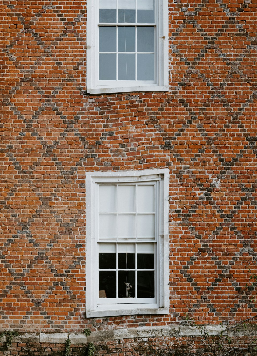 Two stacked white sash windows set in a weathered brick wall.