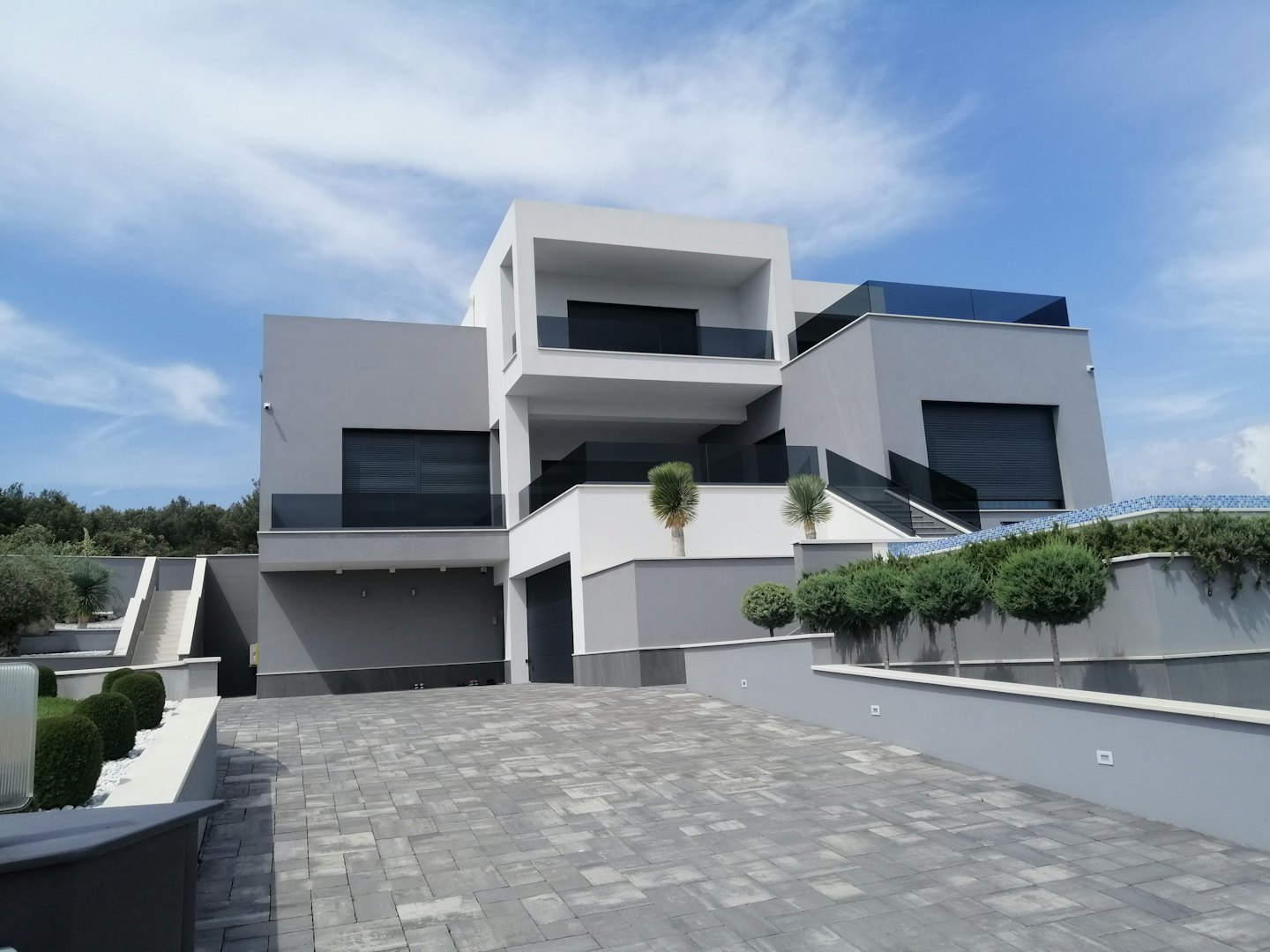 Modern multi-story house with glass balconies and a paved courtyard.