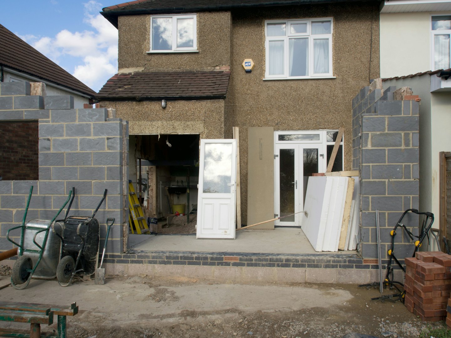 Residential house undergoing renovation with building materials on muddy ground.
