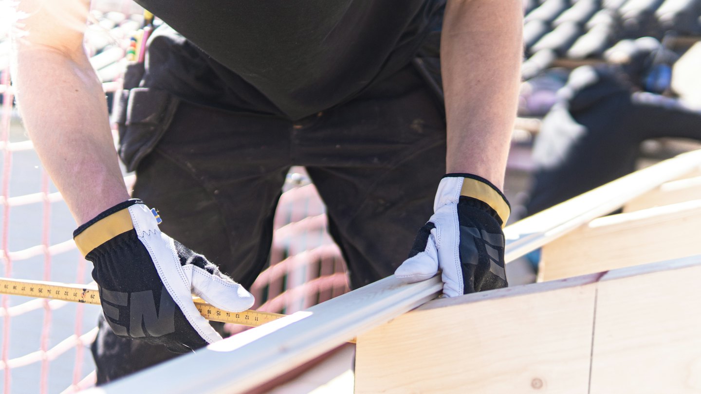 Construction worker measures lumber with a yellow folding ruler.